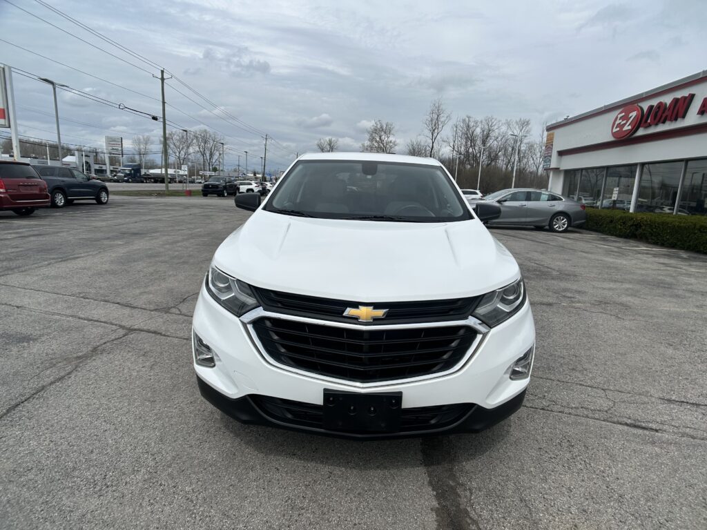 Front view of a white Chevrolet SUV parked in a car lot, dealership building visible in the background.