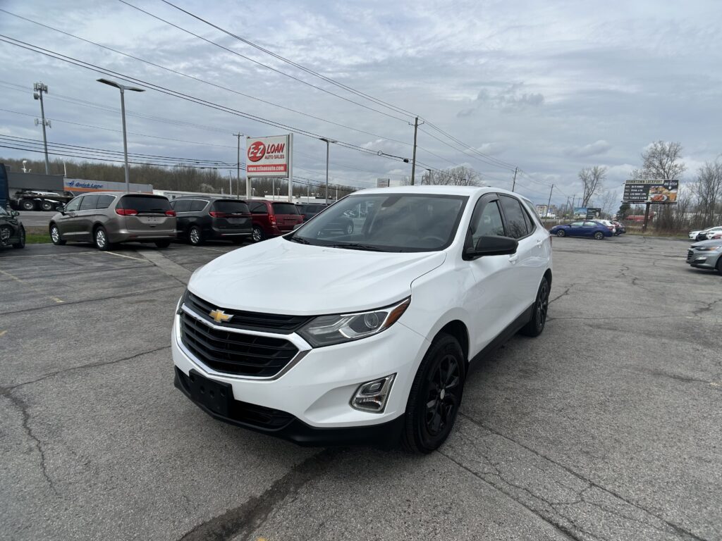 White Chevrolet SUV parked in a dealership lot with other cars and an EZ Loan sign in the background (front-left angled view).