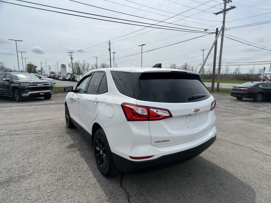 White Chevrolet Equinox SUV parked in a car dealership lot, shown from the rear-left side with other vehicles in the background.