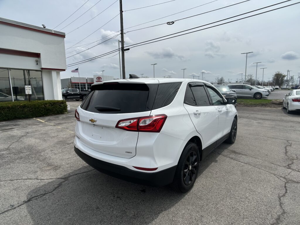 White Chevrolet SUV parked in a dealership lot, rear three-quarter view with a building and flag in the background.