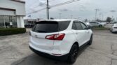 White Chevrolet SUV parked in a dealership lot, rear three-quarter view with a building and flag in the background.
