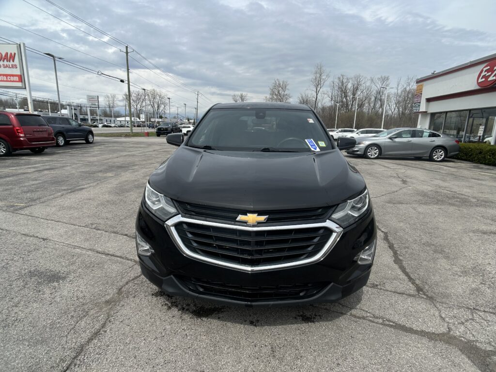 Front view of a black Chevrolet SUV parked in a car dealership lot with other vehicles and a dealership building in the background