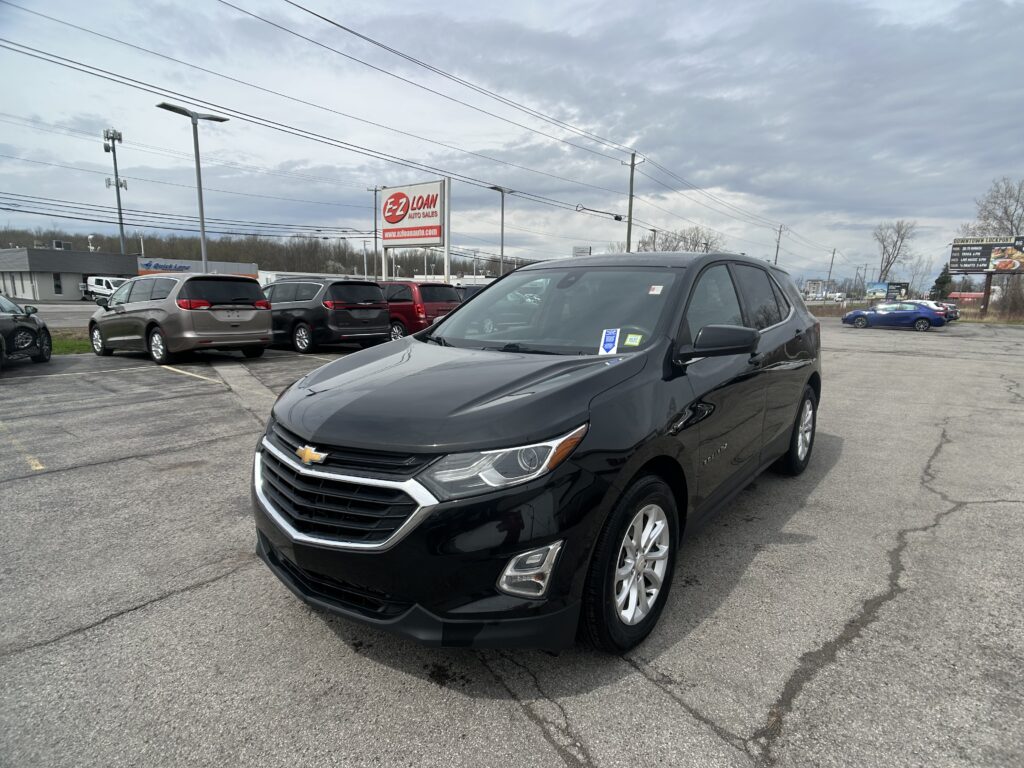 Black Chevrolet SUV parked in a dealership lot with other cars and a sign in the background, front-three-quarter view.