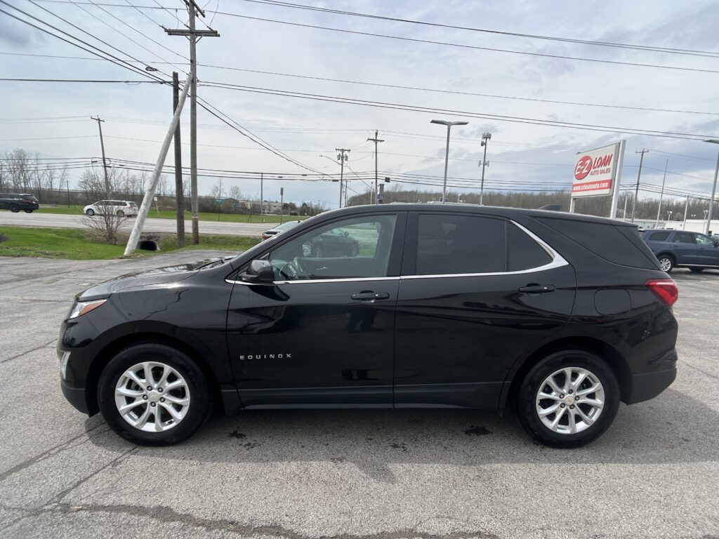 Side view of a black Chevrolet Equinox SUV parked in a dealership lot with a sign and power lines in the background.