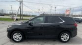 Side view of a black Chevrolet Equinox SUV parked in a dealership lot with a sign and power lines in the background.