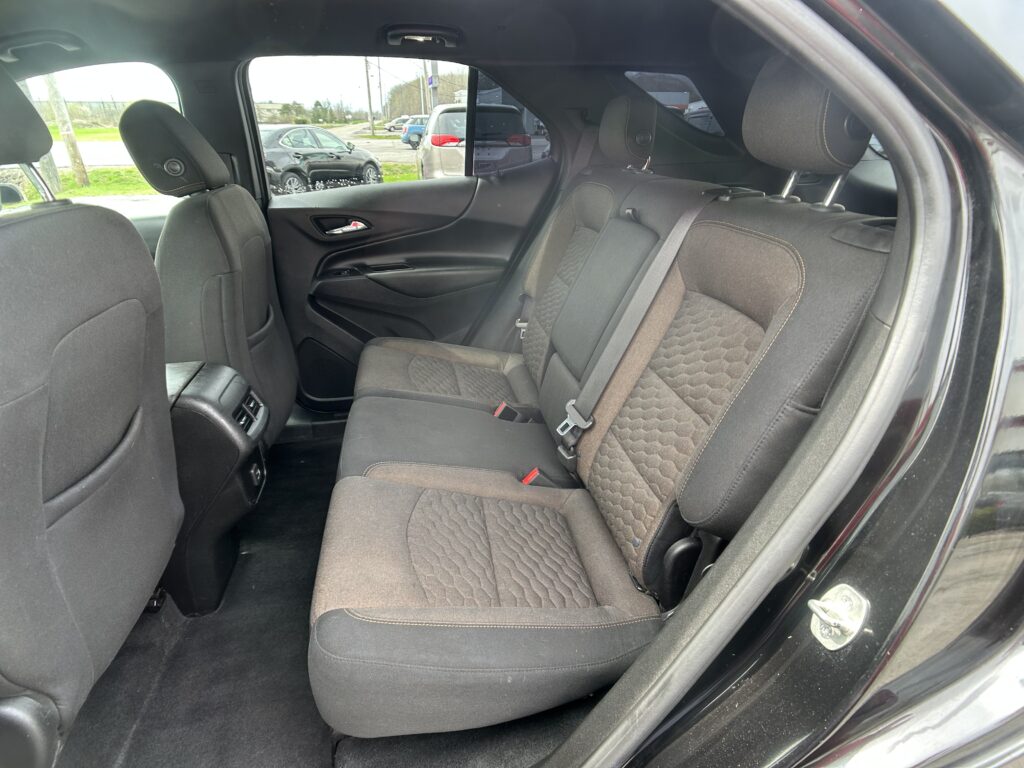 Rear row of a dark cloth car interior with three seats, headrests, and visible seat belts.