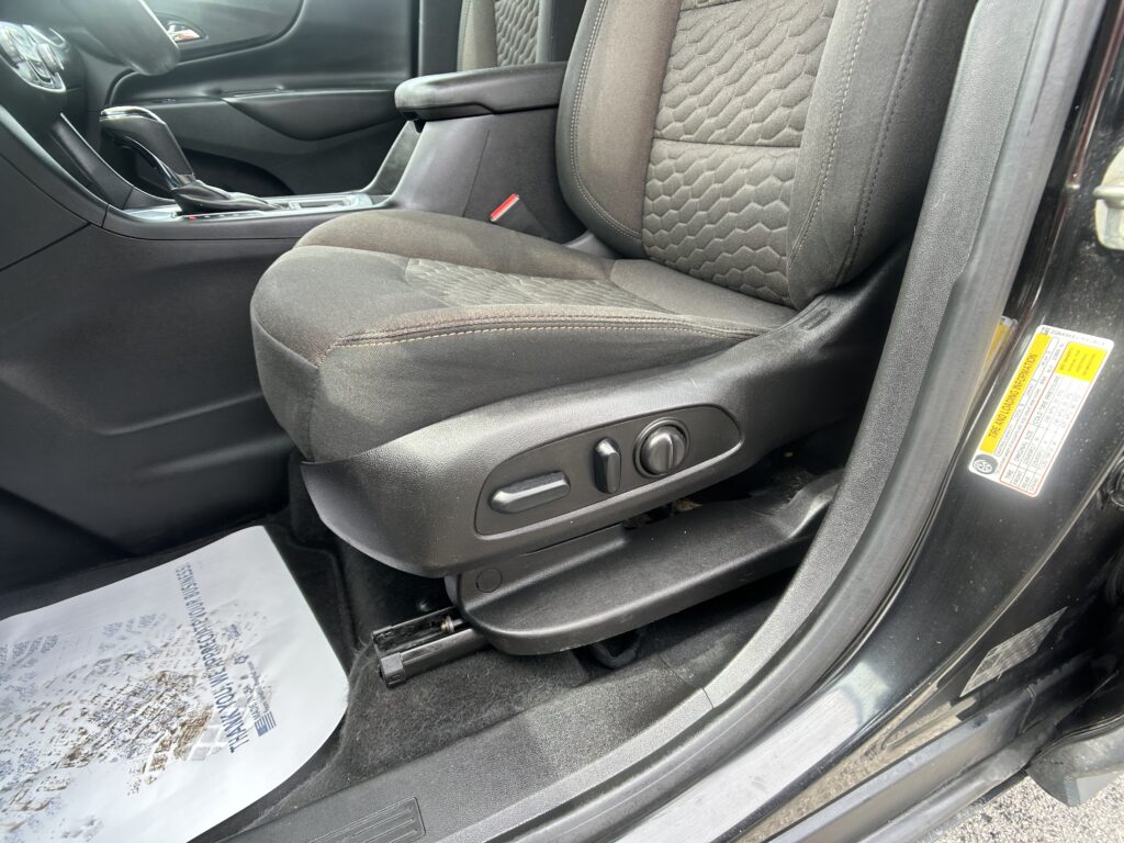 Driver seat with quilted fabric upholstery and side-adjustment controls in a dark car interior.