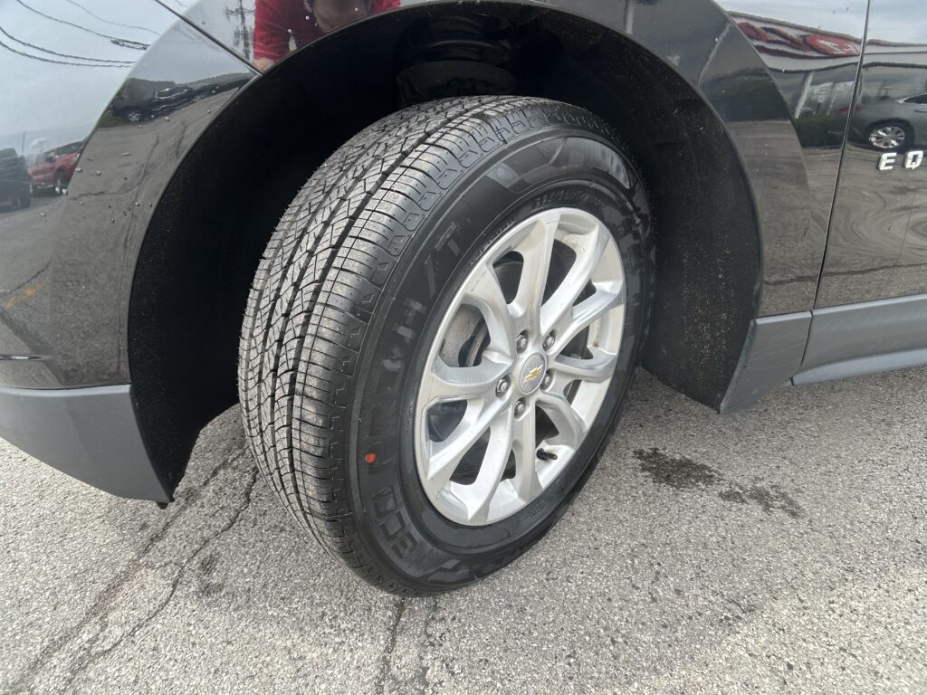 Close-up of a front wheel on a dark gray Chevrolet SUV, showing the treaded tire and alloy rim on pavement.