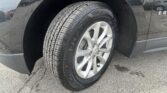 Close-up of a front wheel on a dark gray Chevrolet SUV, showing the treaded tire and alloy rim on pavement.