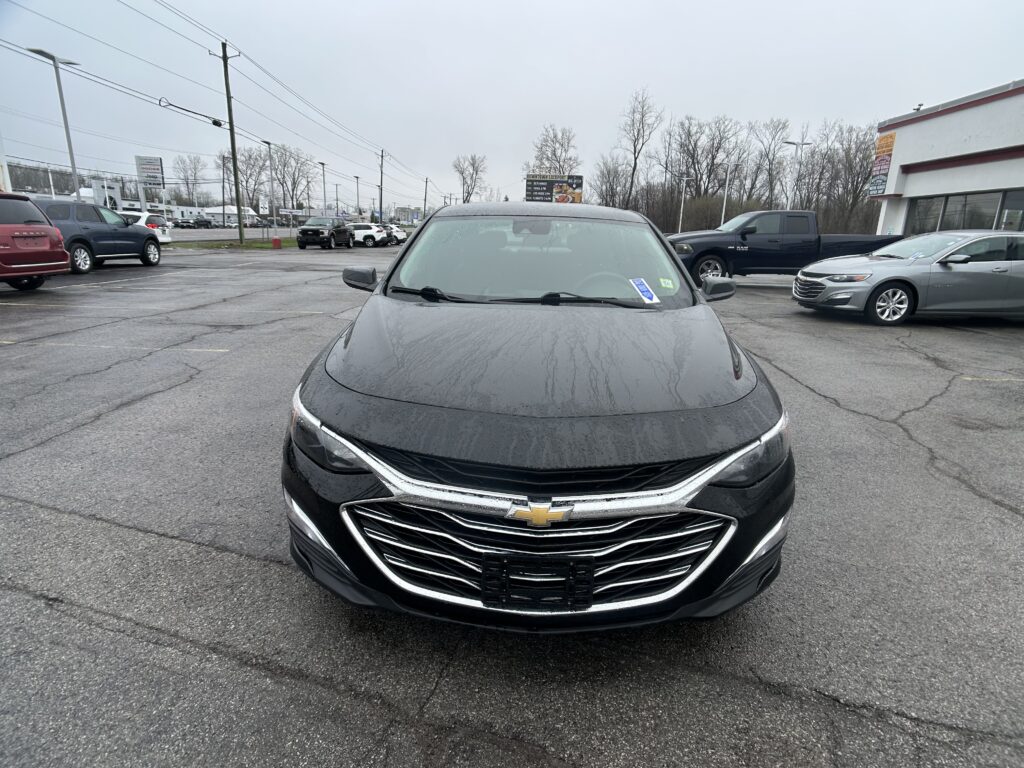 Front view of a black Chevrolet sedan in a wet parking lot, chrome grille with gold bowtie emblem visible.