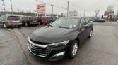 Black Chevrolet sedan parked in a rainy dealership lot with other minivans nearby and an EZ Loan Auto Sales sign in the background.