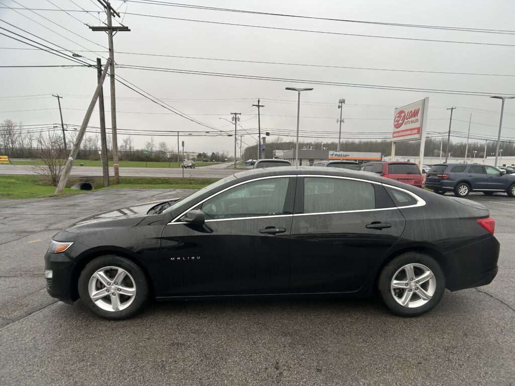 Black Chevrolet Malibu sedan parked in a wet parking lot with a red EZ Loan sign and power lines in the background.