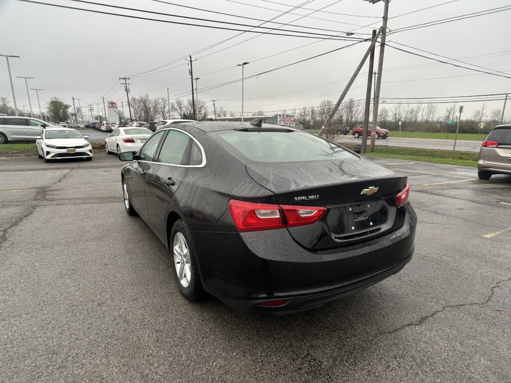 Black Chevrolet Malibu parked in a wet lot, rear view visible with rain droplets on the car.