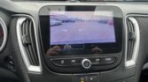 Infotainment screen showing the car's rearview camera view of a parking lot with orange guide lines and distance markers.