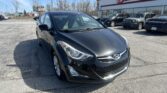 Close-up of a black Hyundai sedan parked in a lot in front of an auto dealership showroom.