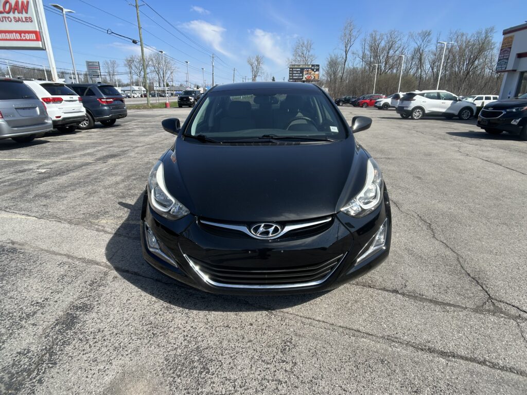 Front view of a black Hyundai in the foreground of a car dealership lot, with several SUVs and a bright blue sky in the background.