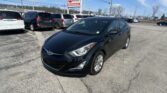 Black Hyundai sedan in the foreground at a car dealership lot with row of minivans behind and an E-Z Loan Auto Sales sign against a blue sky