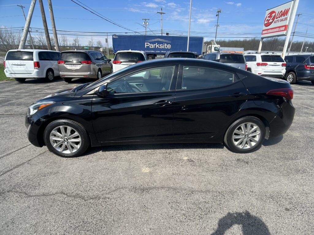 Black sedan in a dealership lot with white vans and a blue Parksite trailer in the background on a sunny day