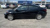 Black sedan in a dealership lot with white vans and a blue Parksite trailer in the background on a sunny day