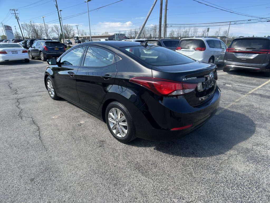 Black Hyundai Elantra in a crowded dealership lot with other vehicles and power lines in the background