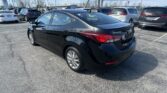 Black Hyundai Elantra in a crowded dealership lot with other vehicles and power lines in the background