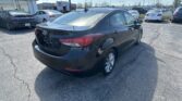 Rear three-quarter view of a dark Hyundai sedan in a car dealership lot with a Toyota showroom in the background.
