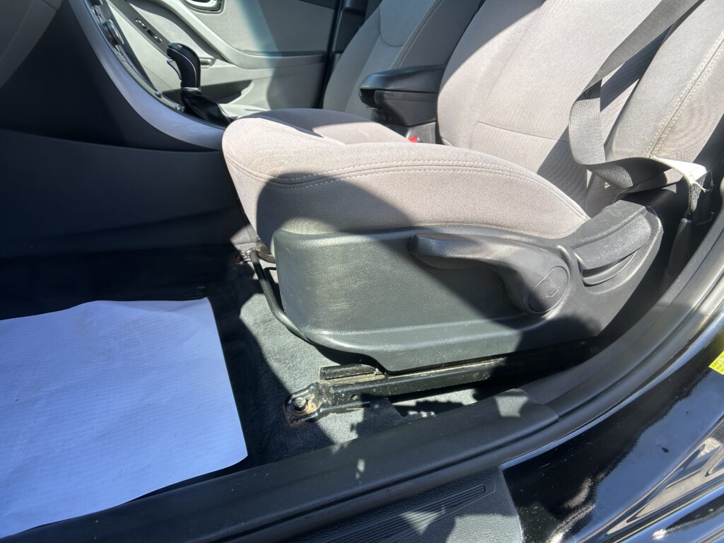 Interior of a car showing the front seats, center console, and seat belt; gear lever nearby on the floor.