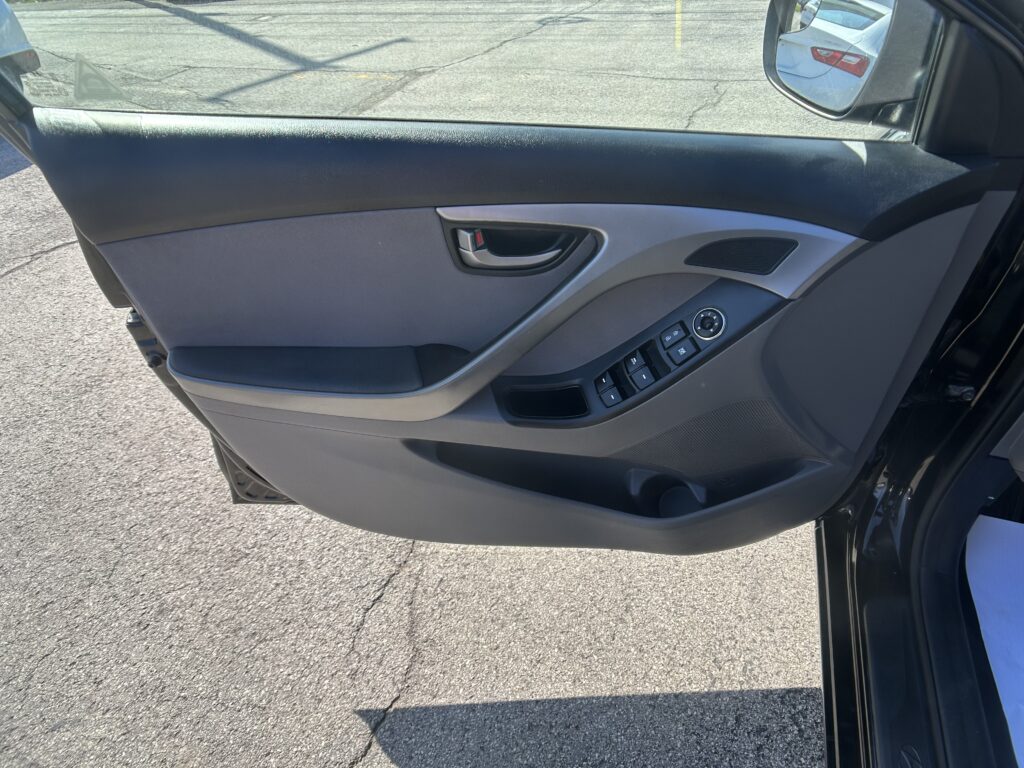 Interior of a car door panel with window controls and side mirror visible through the open window, in a parking lot curbside view