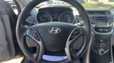 Driver's view of the car interior: steering wheel centered, with instrument cluster and infotainment screen to the right, center console buttons visible.]