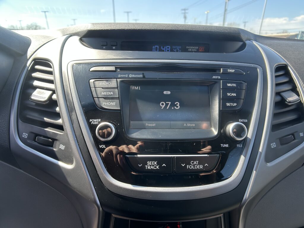 Center console car stereo with FM radio display showing 97.3 and outside temp 47°F; surrounding buttons for Radio, Media, Phone and Mute/Scan.