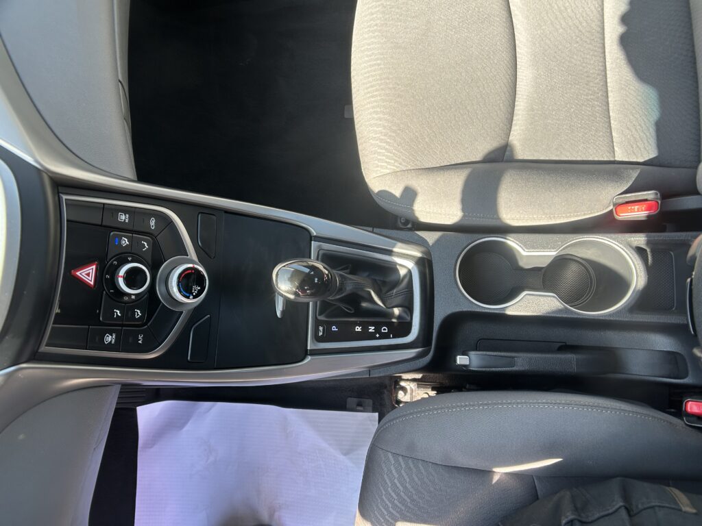 Car interior with gear shifter and climate controls; a white sheet of paper on the floor by the driver.
