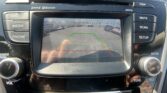 In-dash rearview camera display with colored guide lines (green, yellow, red) and surrounding parked cars behind the vehicle.