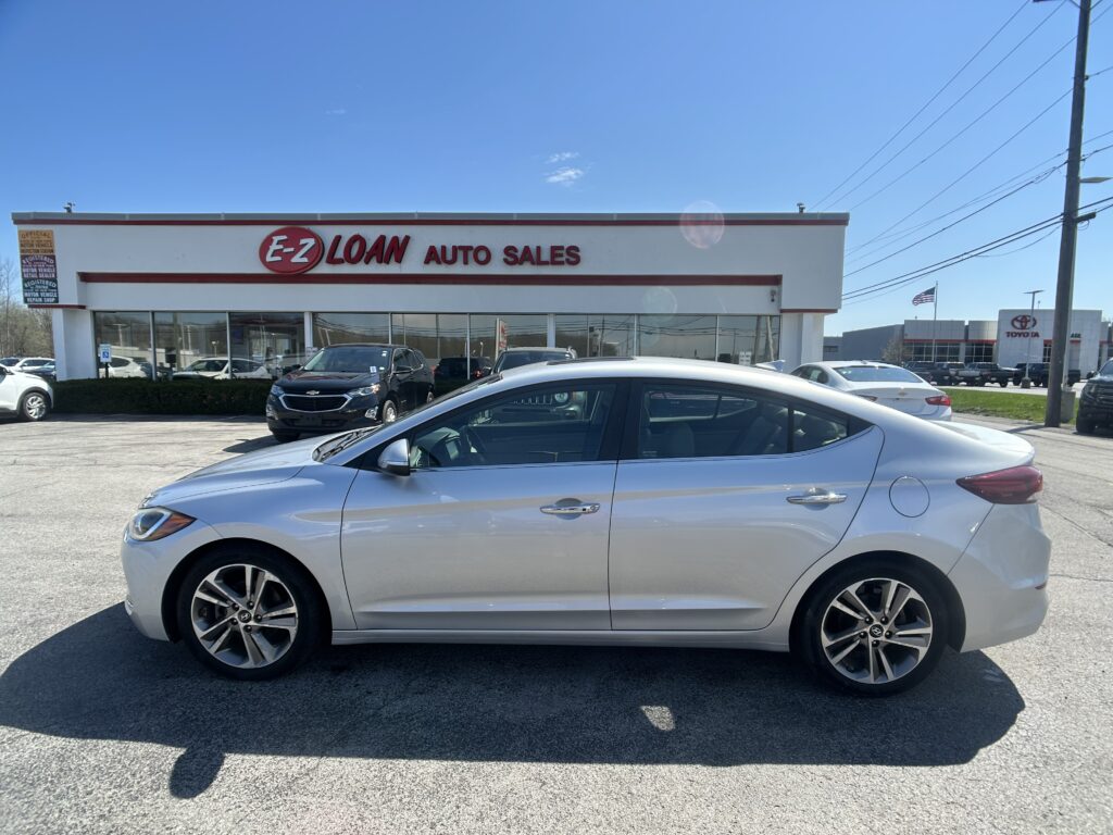 Front view of a silver sedan in the dealership lot in front of EZ Loan Auto Sales, with the building sign and other cars in the background under a blue sky.