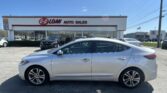 Front view of a silver sedan in the dealership lot in front of EZ Loan Auto Sales, with the building sign and other cars in the background under a blue sky.