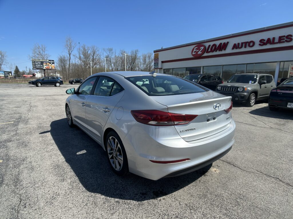 Rear three-quarter view of a silver Hyundai Elantra in a car dealership lot with the EZ Loan Auto Sales building in the background.