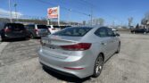 Silver Hyundai sedan foreground in a car lot under a blue sky with other vehicles and an EZ LOAN Auto Sales sign in the background.