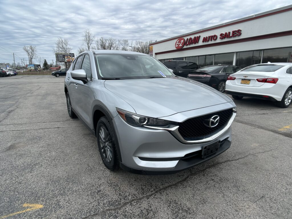 Silver Mazda SUV in the foreground at an auto dealership with the E-LOAN Auto Sales building in the background and other cars nearby.