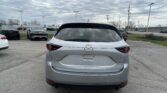 Rear view of a silver Mazda CX-5 in a parking lot with other cars and a cloudy sky above.