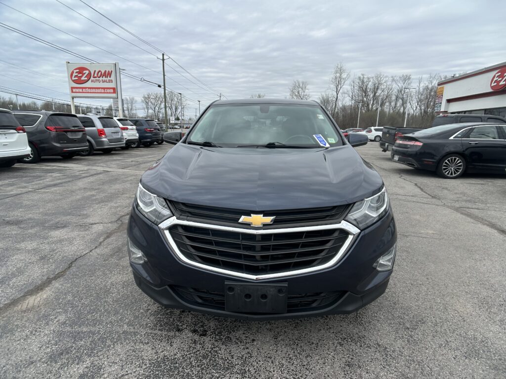 Front view of a dark Chevrolet SUV at a used-car lot, with an E-Z LOAN Auto Sales sign visible in the background.