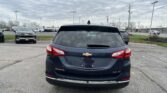Rear view of a dark Chevrolet Equinox in a parking lot, with other cars and a cloudy sky in the background.