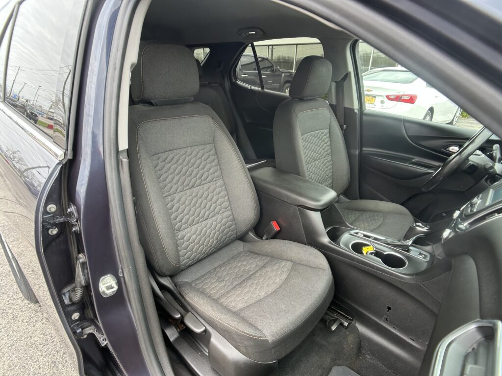 Front interior of a dark car with two cloth seats and visible stitching, center console between them.