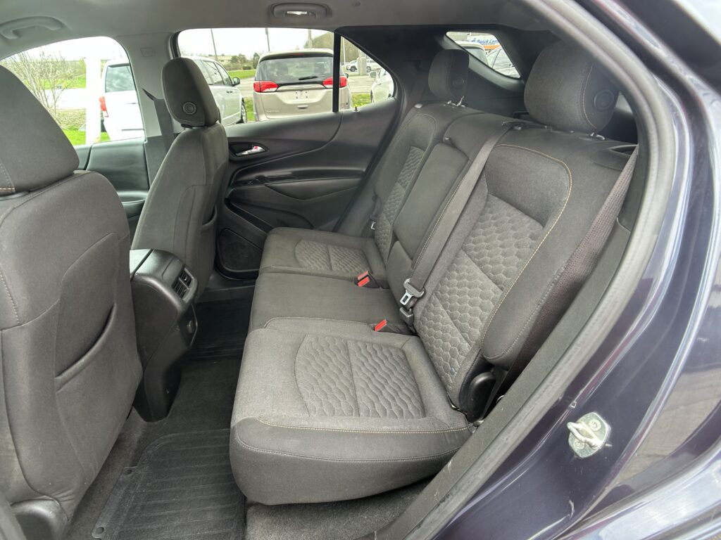 Rear passenger seats in a dark fabric car interior with center and side seatbelts visible and front seatbacks in view.