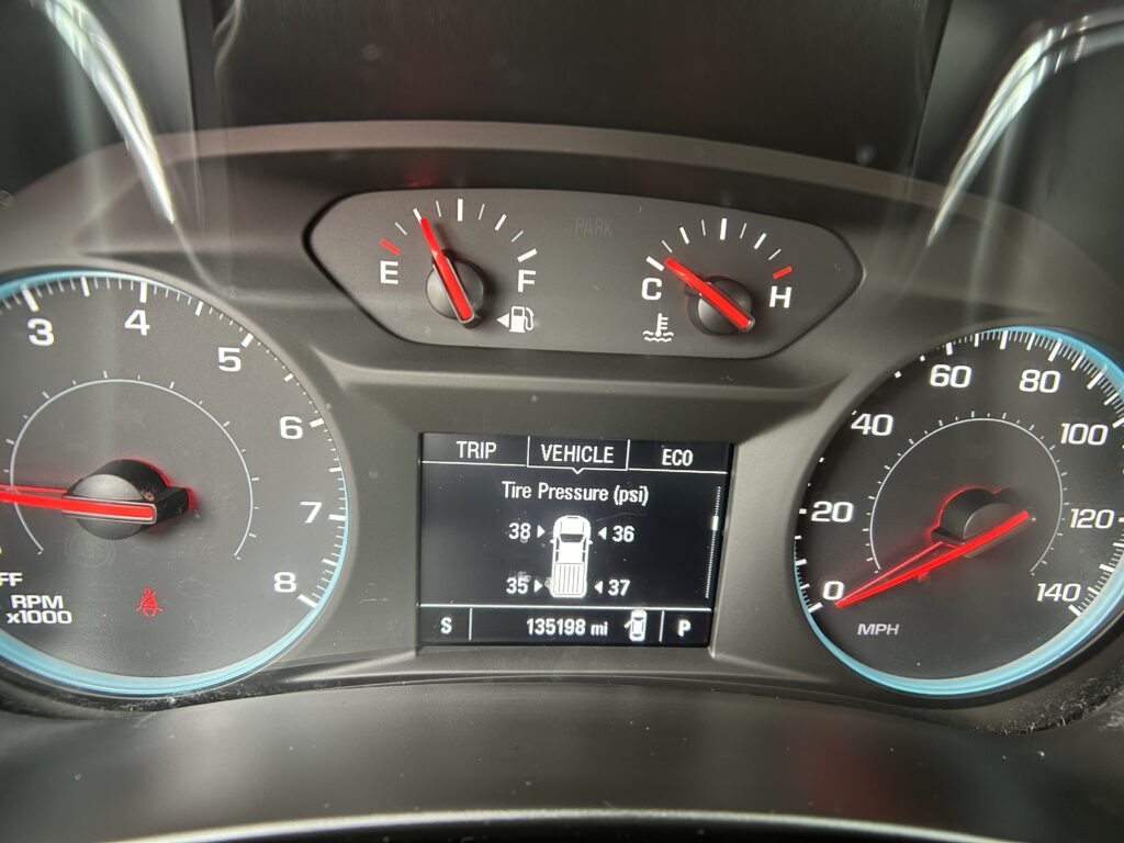 Vehicle instrument cluster showing tachometer (left) and speedometer (right) with red needles, and a central digital display.