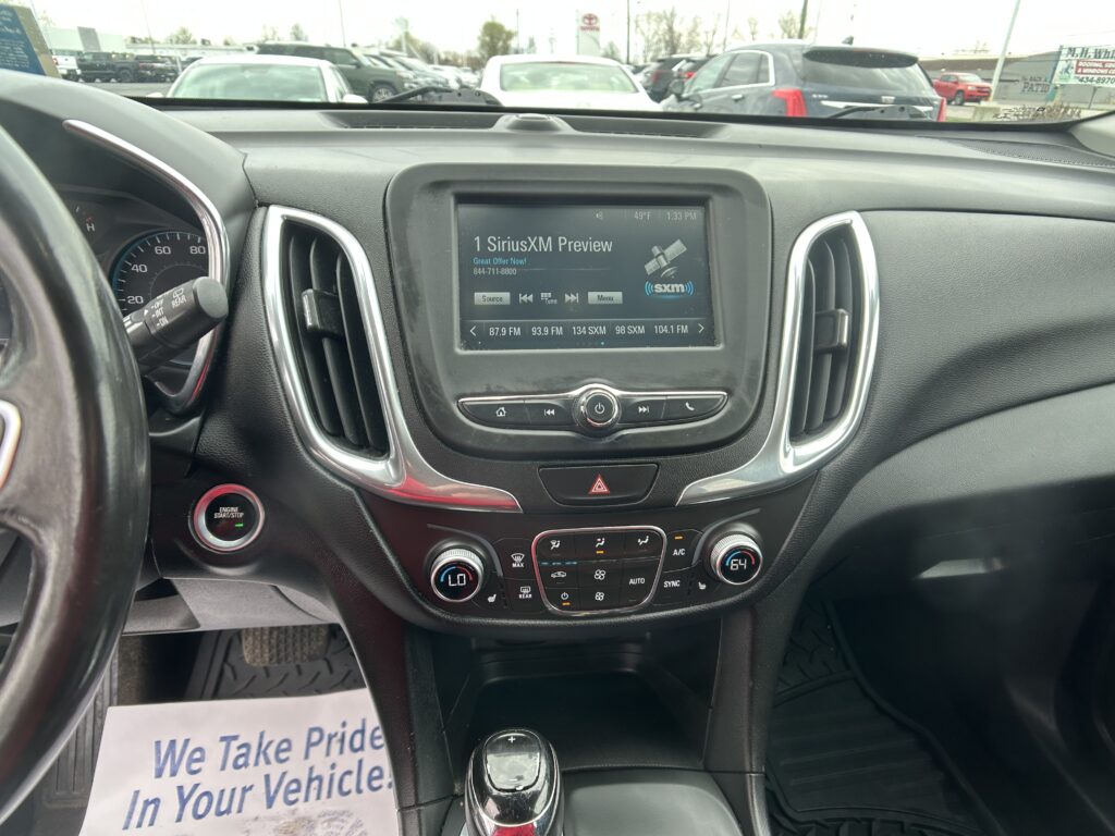 Car interior dashboard with a touchscreen showing SiriusXM Preview, centered between air vents, and a gear shifter below.