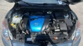 Open hood showing engine bay of a Mazda with a bright blue engine cover and surrounding components like coolant reservoir and hoses.