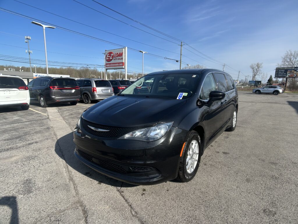 Front black minivan in a crowded car lot with a blue sky and an EZ LOAN Auto Sales sign in the background.
