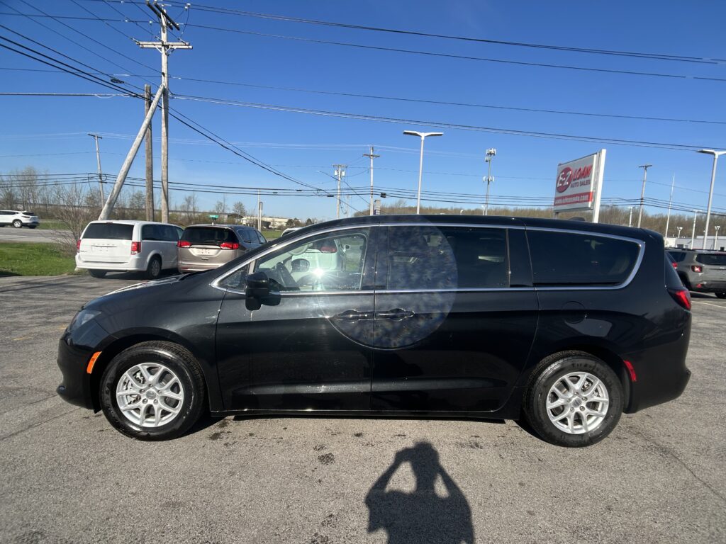 Black SUV in foreground at a car dealership lot with power lines and utility poles in clear blue sky behind. A sign for auto sales is visible in the distance.