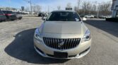 Beige Buick SUV seen from the front in a dealership lot with other cars and leafless trees in the background.”