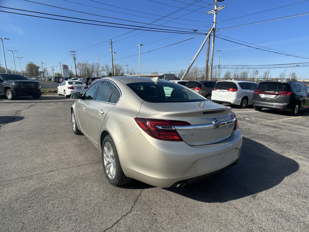 Parking lot full of cars at a dealership, with a white Buick in the foreground and power lines overhead against a blue sky.