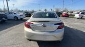 Rear view of a silver Buick Regal in a crowded car dealership lot with multiple parked cars under a blue sky.